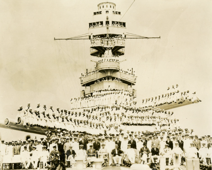 Historical group portrait of USS Arizona officers and crew assembled on deck, gun barrels, and superstructure.